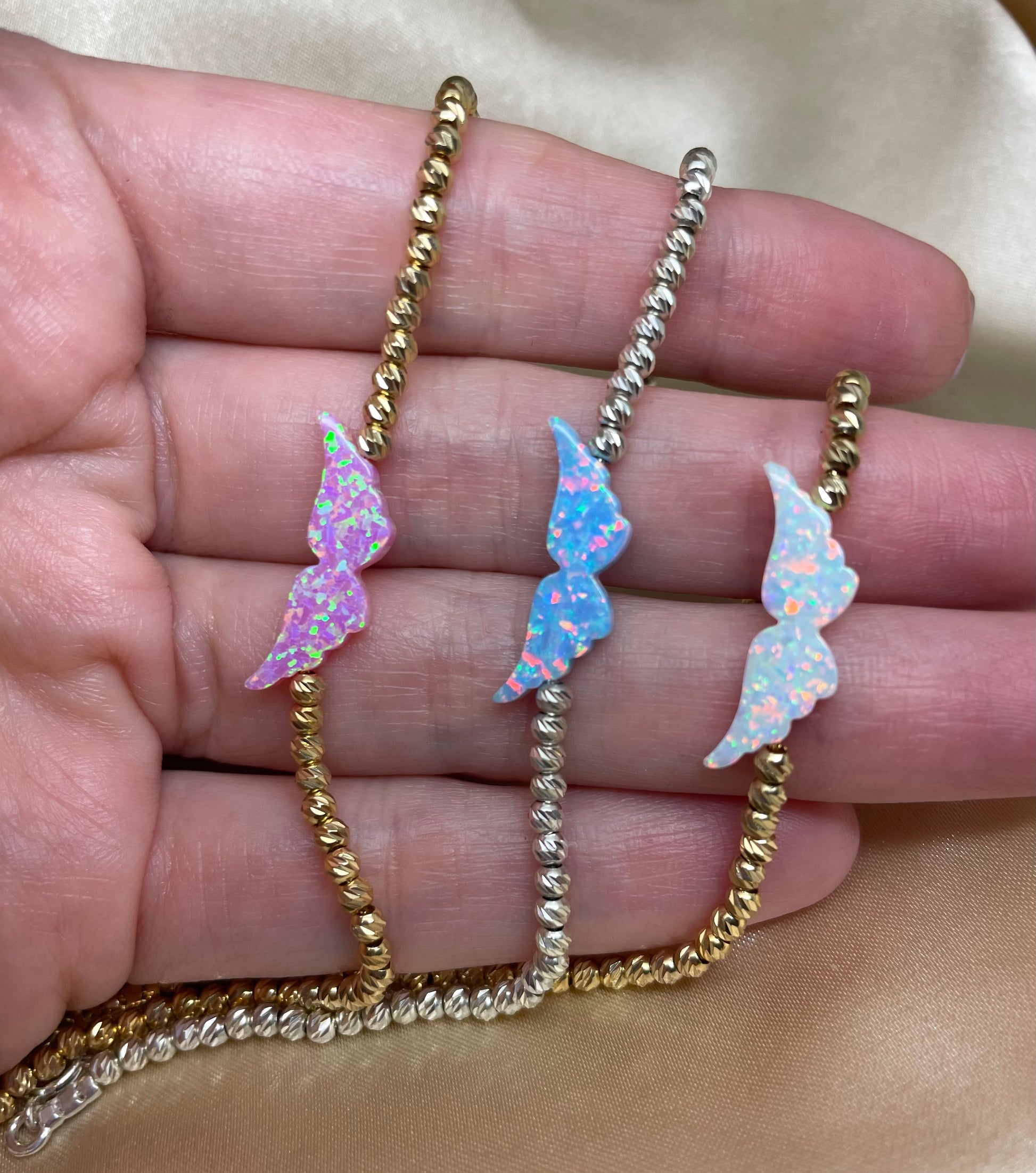 An opal angel wing bracelet with hand-strung beads on a person's hand, displaying the delicate design and the shimmering opal charm.