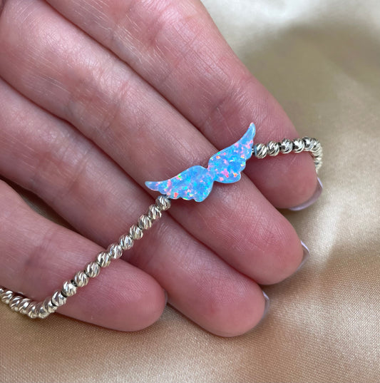 An opal angel wing bracelet with hand-strung beads on a person's hand, displaying the delicate design and the shimmering opal charm.