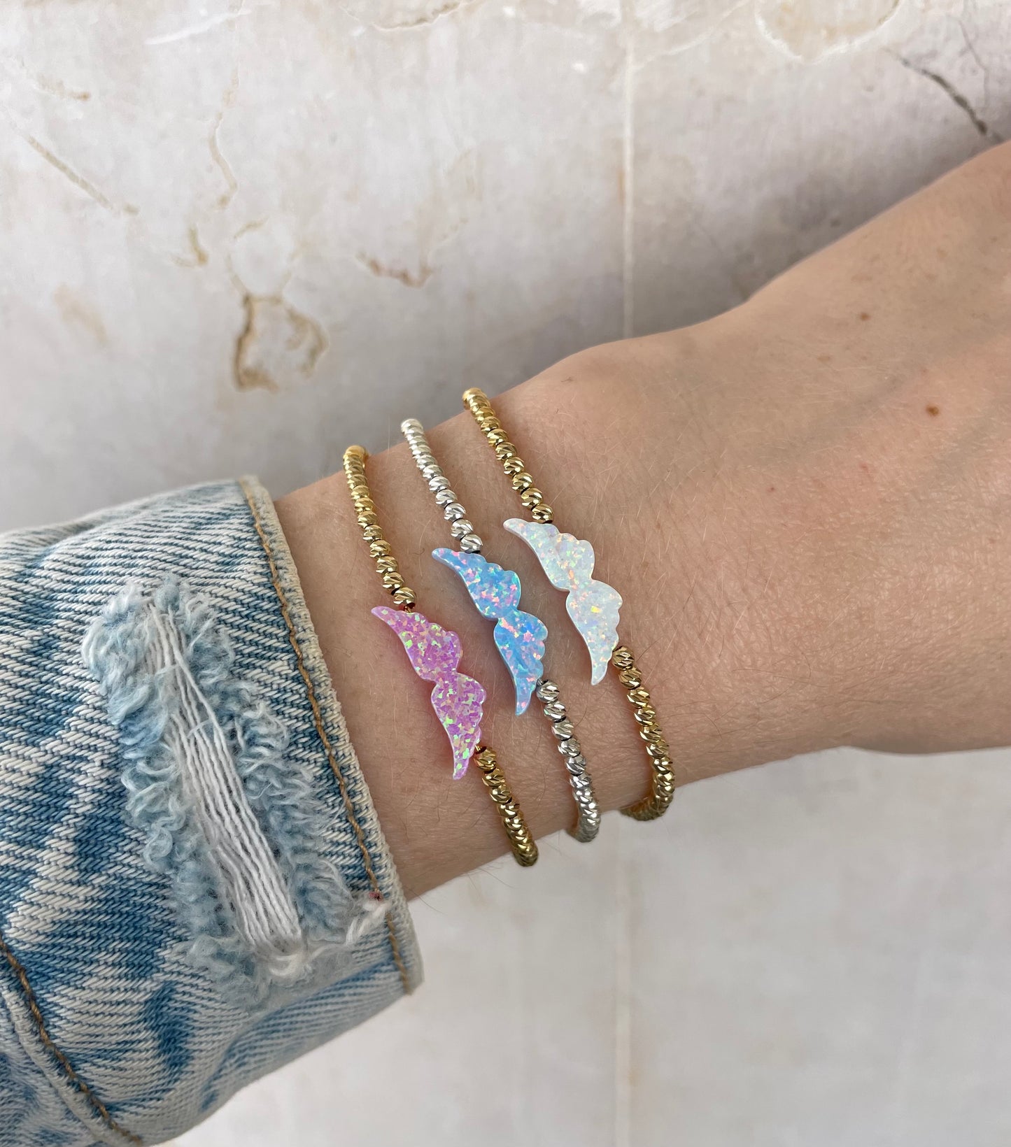 An opal angel wing bracelet with hand-strung beads on a person's hand, displaying the delicate design and the shimmering opal charm.
