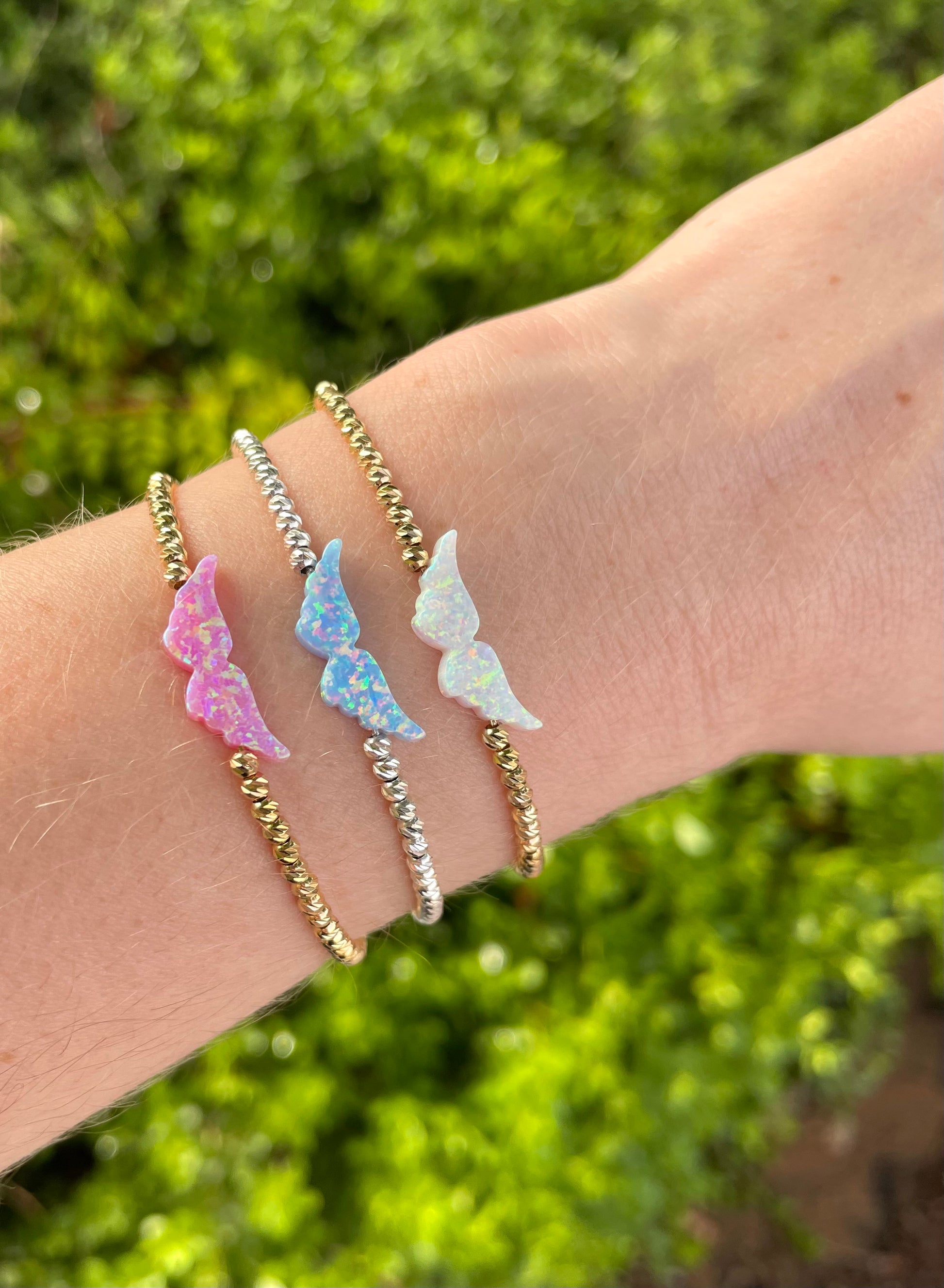 An opal angel wing bracelet with hand-strung beads on a person's hand, displaying the delicate design and the shimmering opal charm.