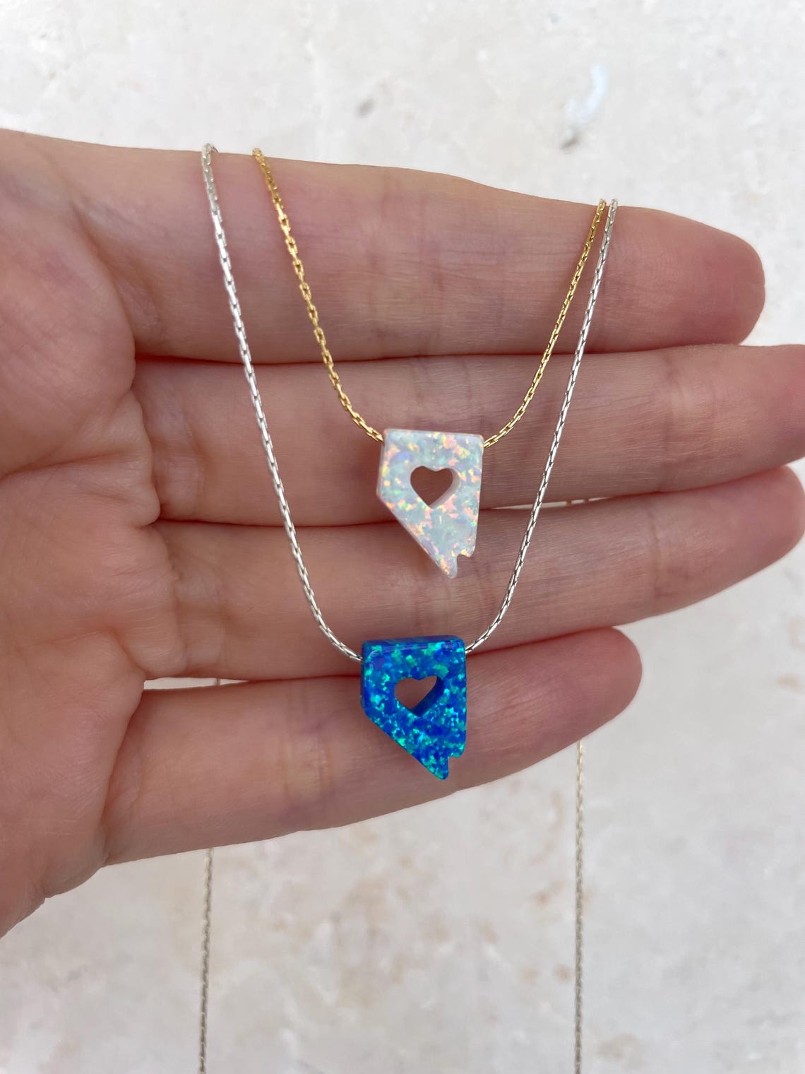 Two heart-shaped pendants on gold and silver chains held in a hand.