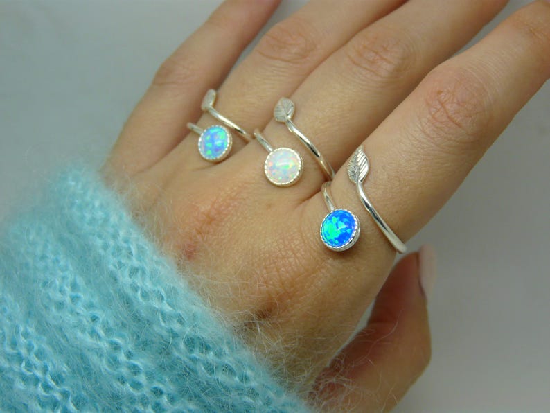 Hand wearing three silver rings with opal stones on a plain background