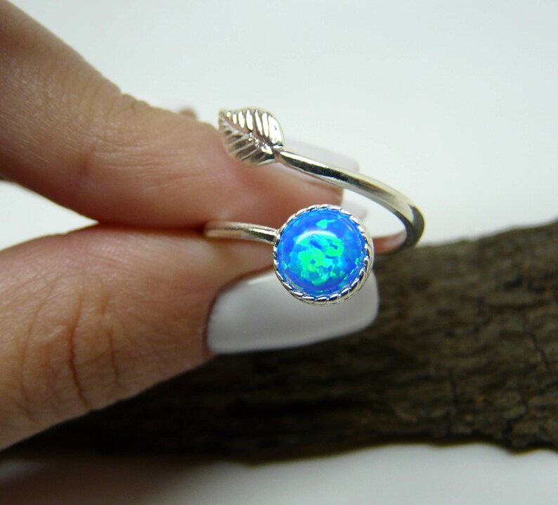 Silver ring with a blue opal stone on a finger against a white background