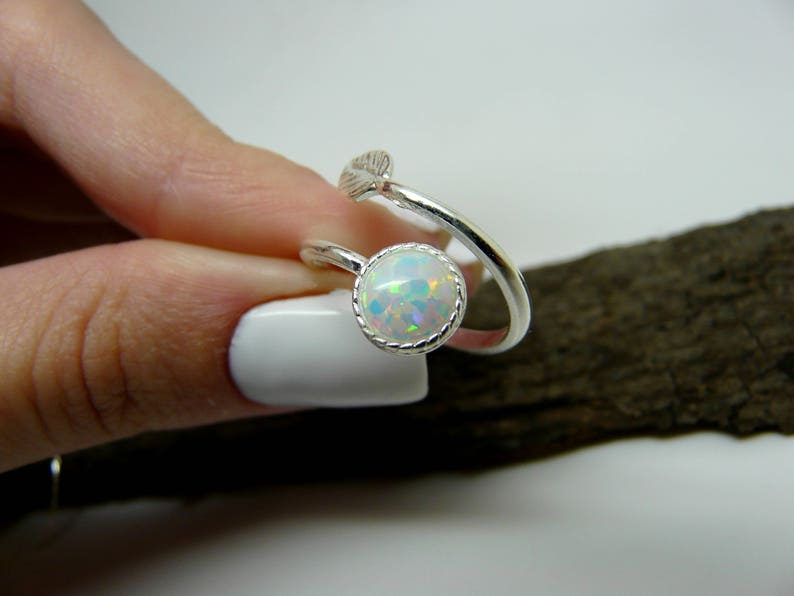 Silver ring with a round opal stone on a hand with white nail polish.
