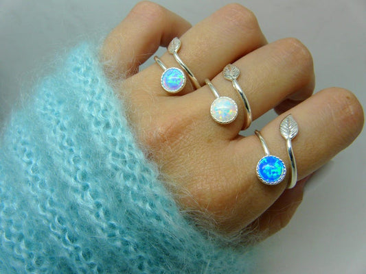 Hand wearing multiple silver rings with gemstones on a light blue textured fabric background