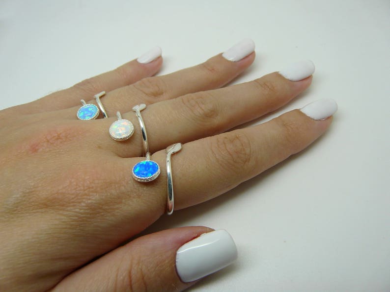 Hand wearing three silver rings with colorful gemstones on a white background