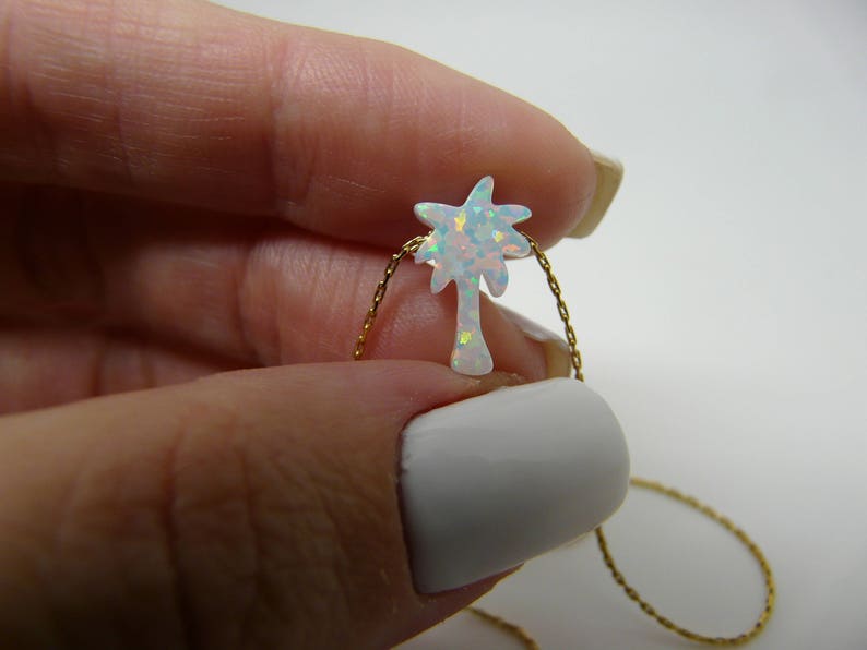 Hand holding opal tree pendant on a gold chain