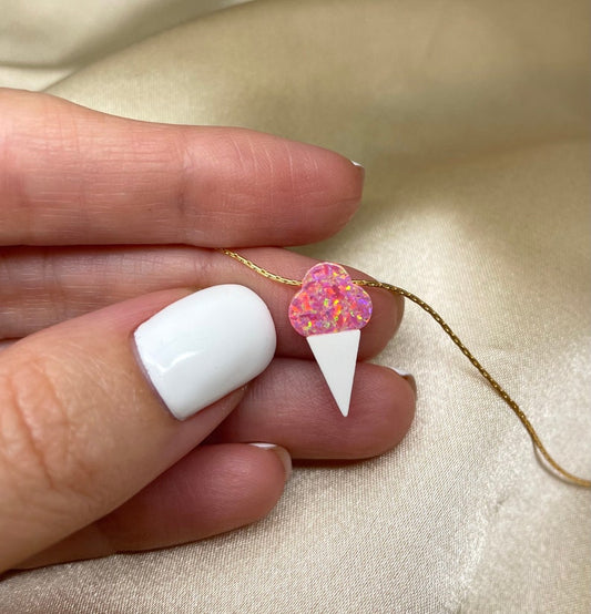 A hand holding a sterling silver necklace with a gold-filled ice cream pendant with a sprinkle topping.