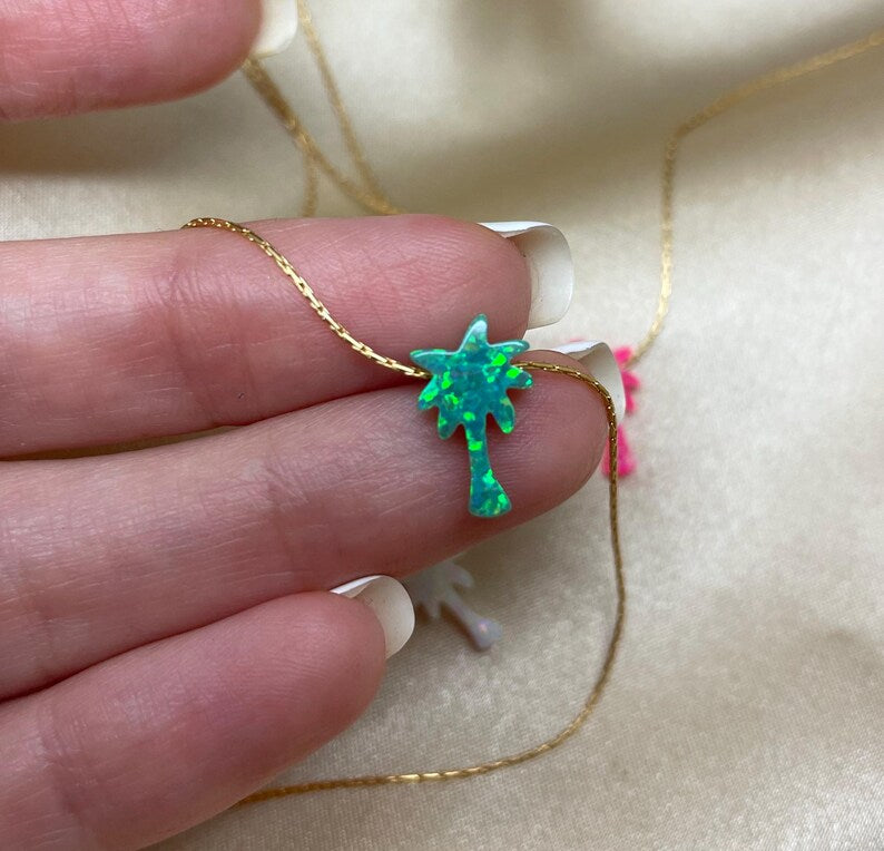Hand holding opal tree pendant on a gold chain