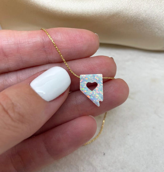 Opal heart-shaped pendant on a gold chain held by a hand with white nail polish.