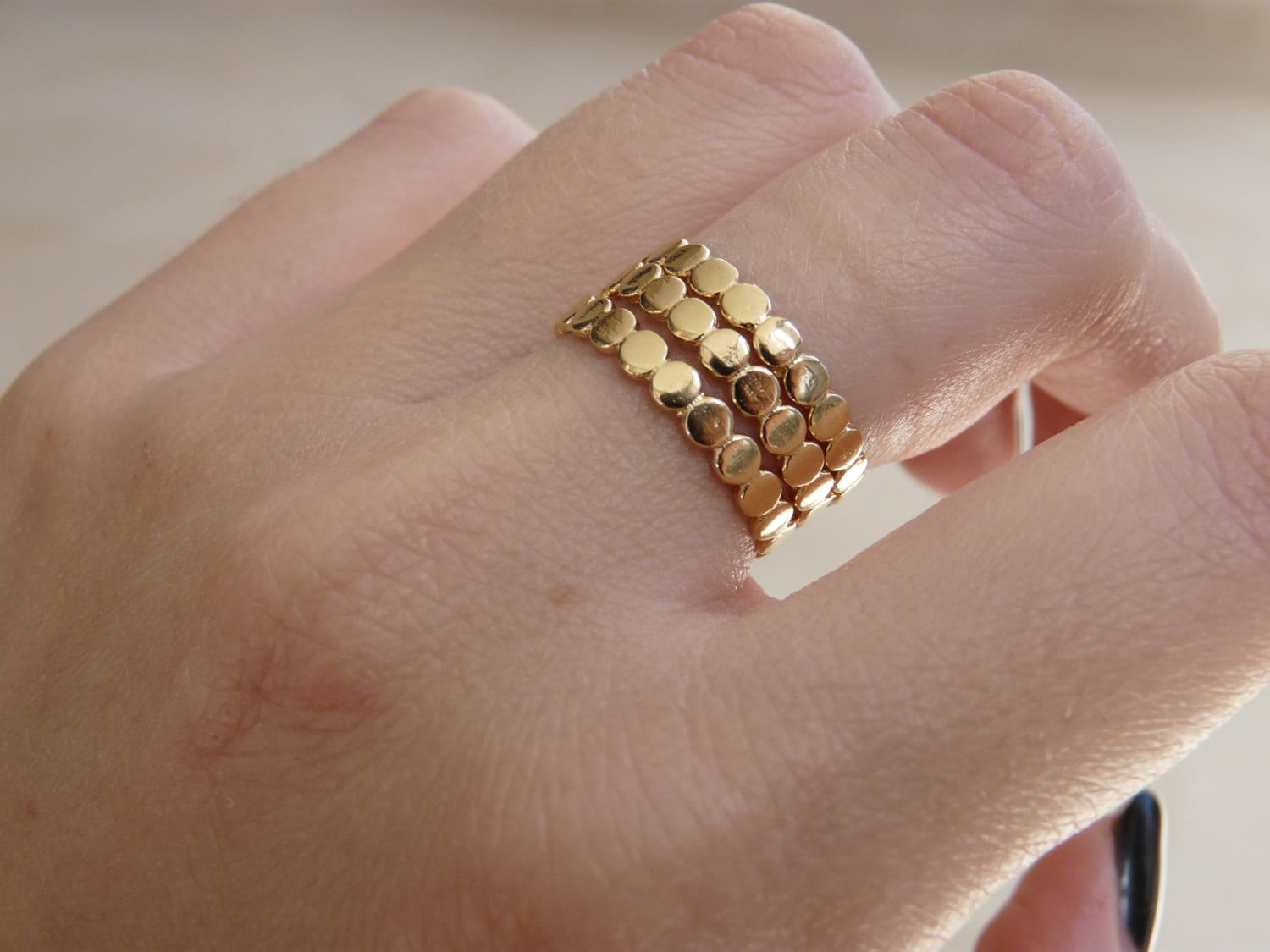 A close-up image of a person's finger wearing multiple gold stacking rings with a textured surface.