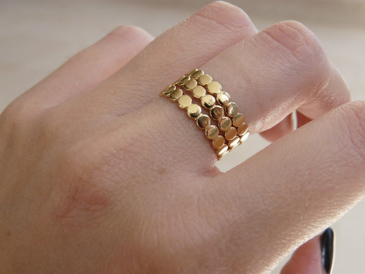 A close-up image of a person's finger wearing multiple gold stacking rings with a textured surface.