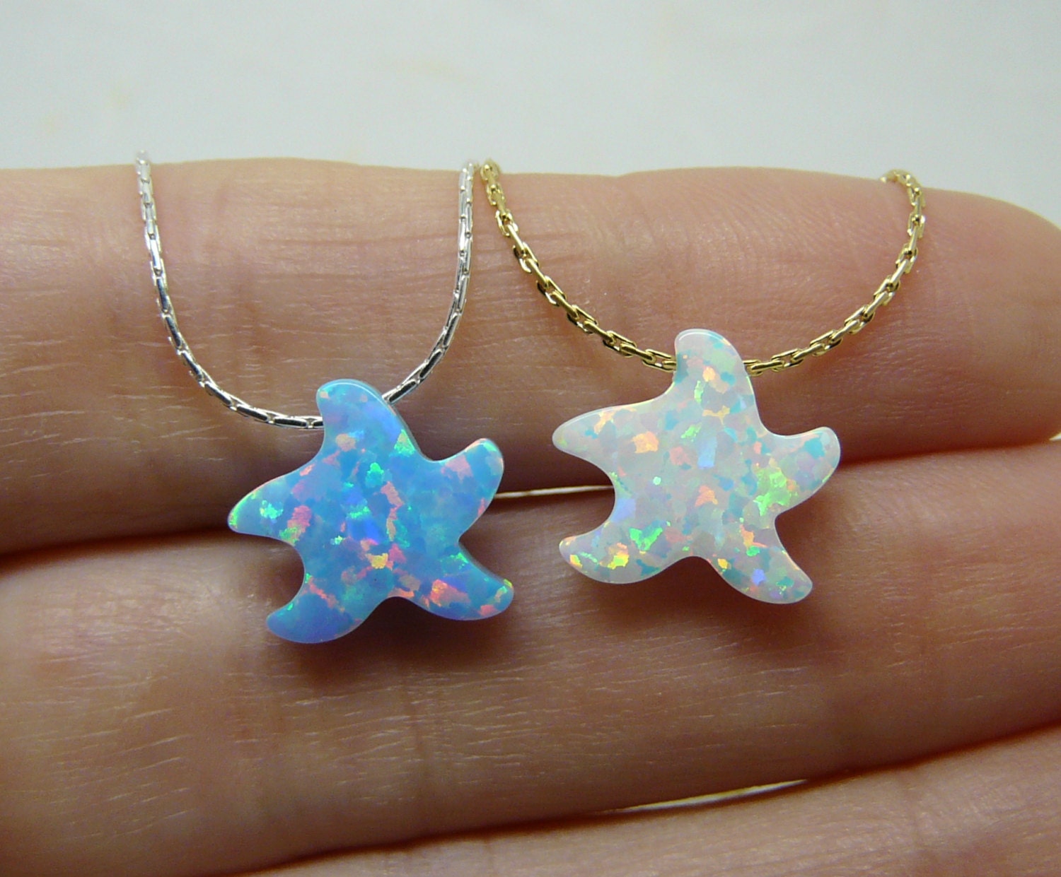 Two opal starfish pendants on gold chains, displayed on a hand.