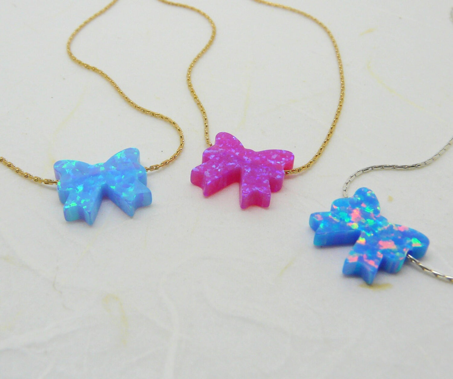 A collection of bow necklaces with opal pendants in blue and pink colors, displayed on a light background.