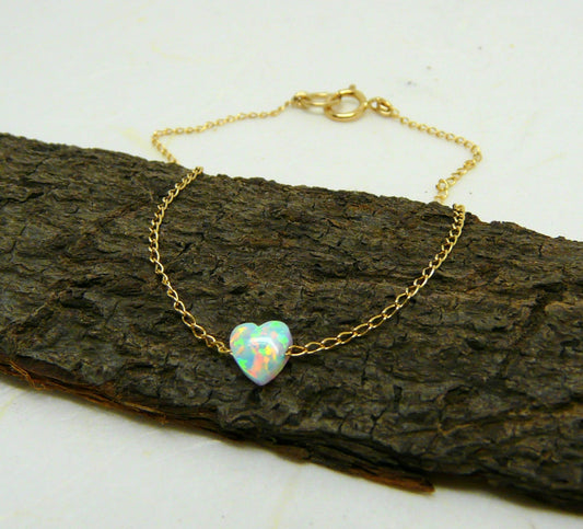A delicate Opal Heart Bracelet with a gold-filled chain and a heart-shaped opal charm, displayed on a wooden surface.