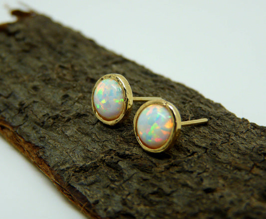 A pair of gold-filled stud earrings with opal stones, displayed on a wooden surface.