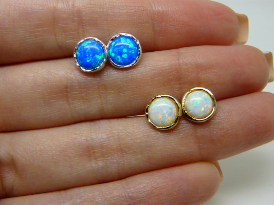 A pair of opal stud earrings in gold-filled settings, displayed on a hand.
