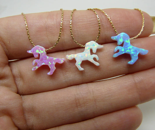 A selection of opal unicorn pendants on gold-filled chains, displayed on a hand.