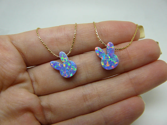 Two opal bunny necklaces, one in gold and one in silver color, displayed on a person's hand.