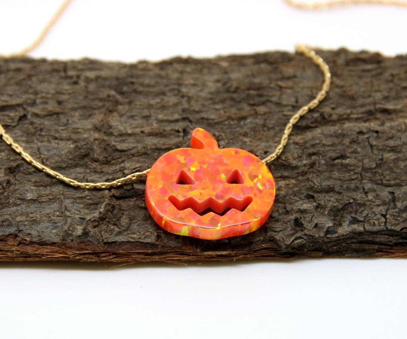 An opal pumpkin charm necklace displayed on a wooden surface.