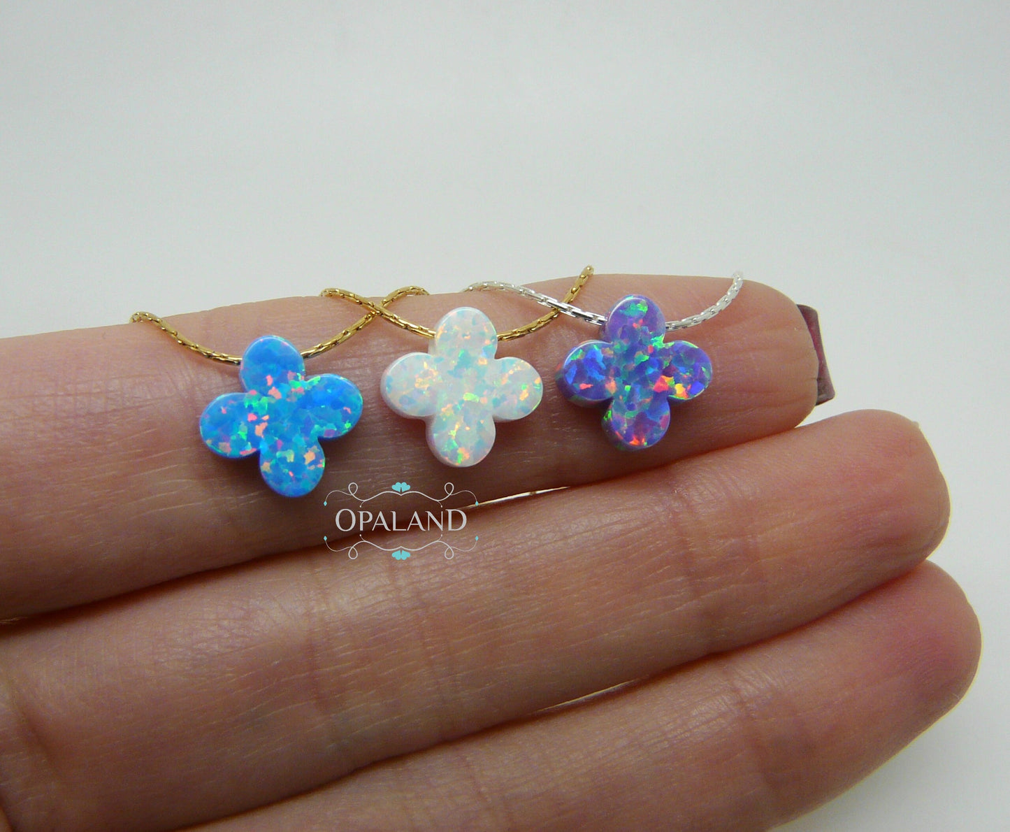 Three opal clover pendants on gold chains, displayed on a hand.