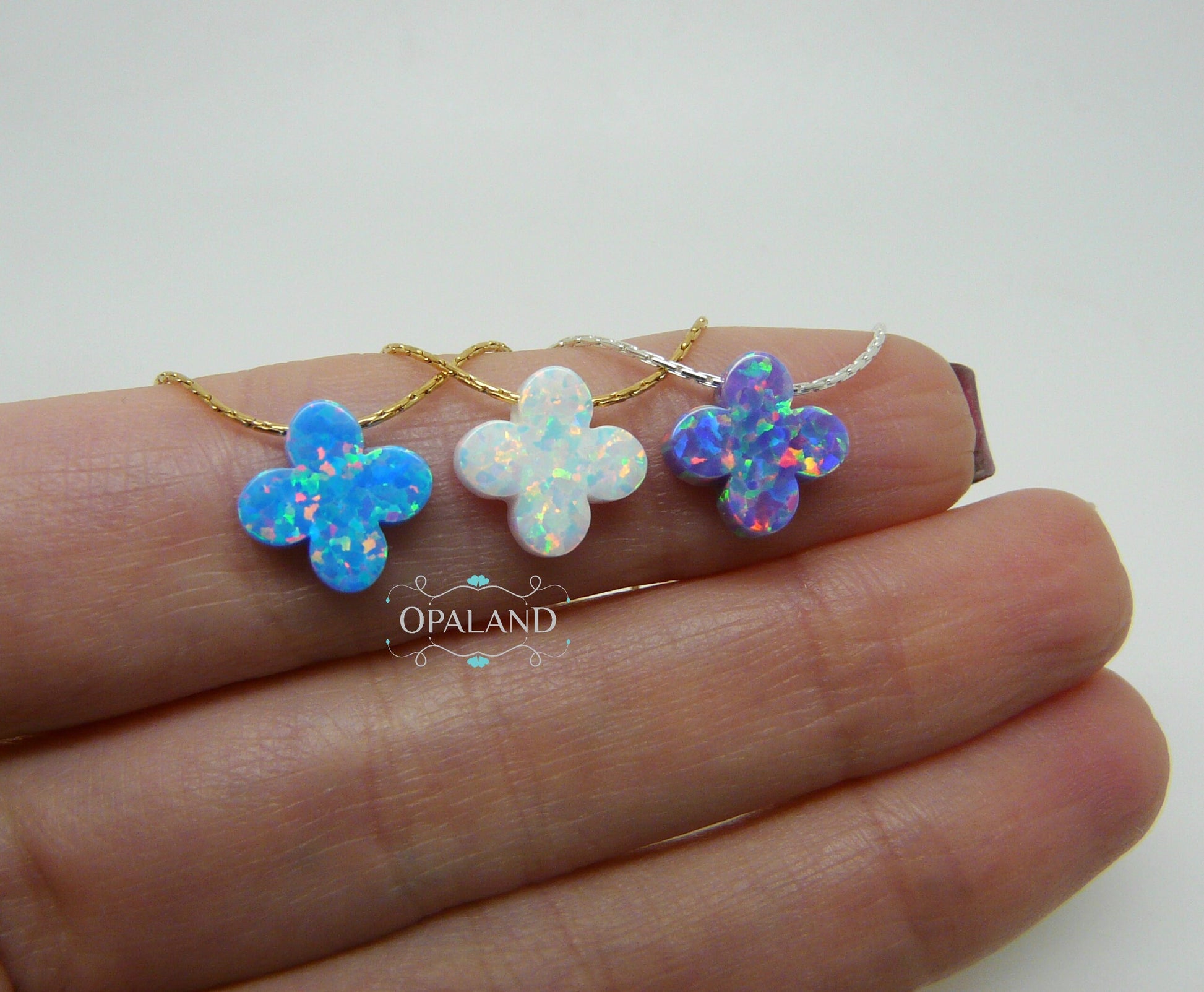 Three opal clover pendants on gold chains, displayed on a hand.