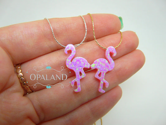 A hand holding a pink opal flamingo pendant necklace with a gold-filled chain.