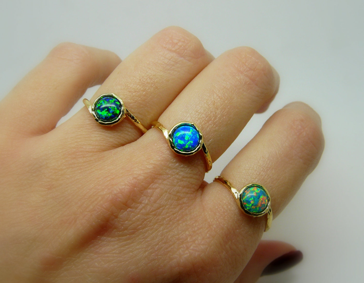 A set of three gold-filled rings with opal stones, displayed on a hand, showcasing the rings from different angles.