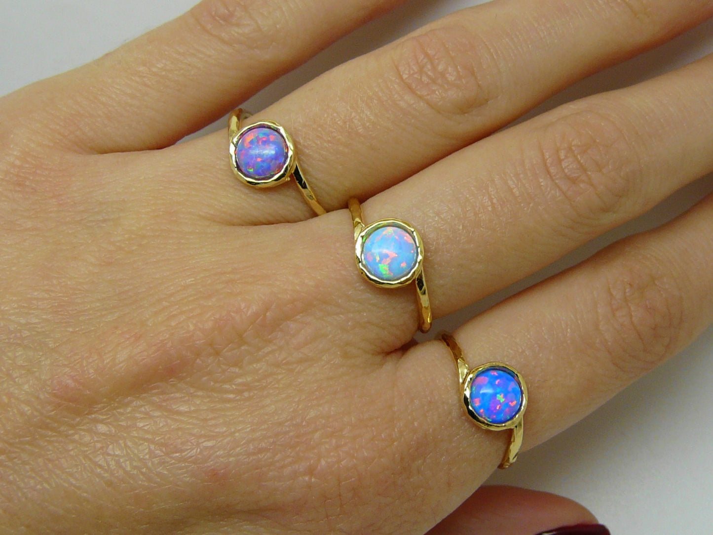 A close-up of a person's hand showcasing three gold filled opal rings on each finger.