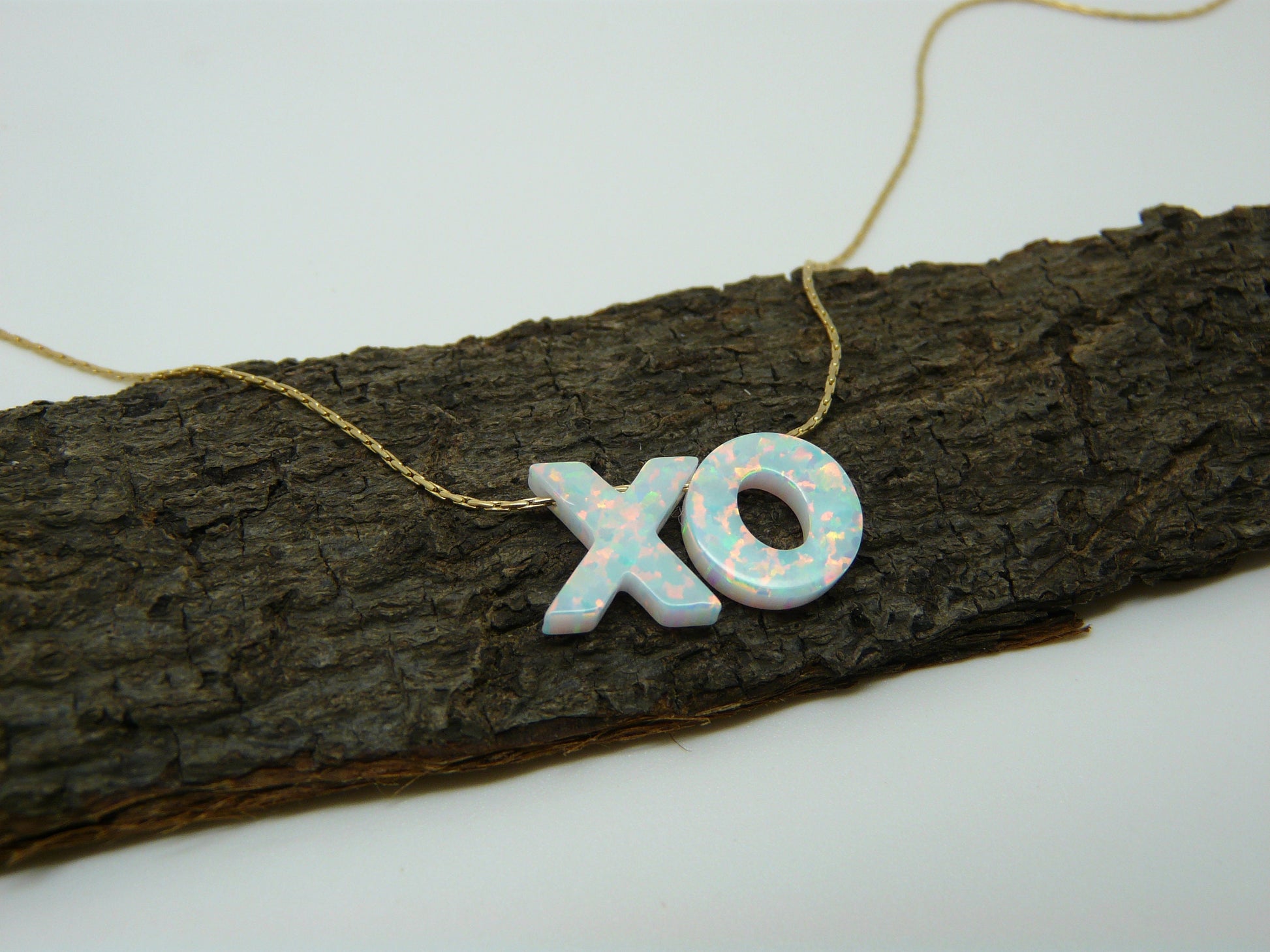 A necklace with the letters 'XO' made of opal beads laid out on a wooden branch.
