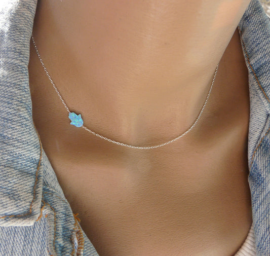 A dainty opal Hamsa necklace displayed on a person's neck, showcasing its delicate design and the blue opal pendant.