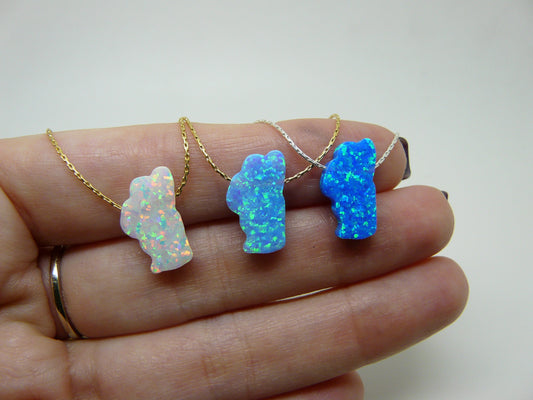 A hand holding three opal charms with varying shades of blue and white, set on gold-filled mountings, in preparation for making necklaces.