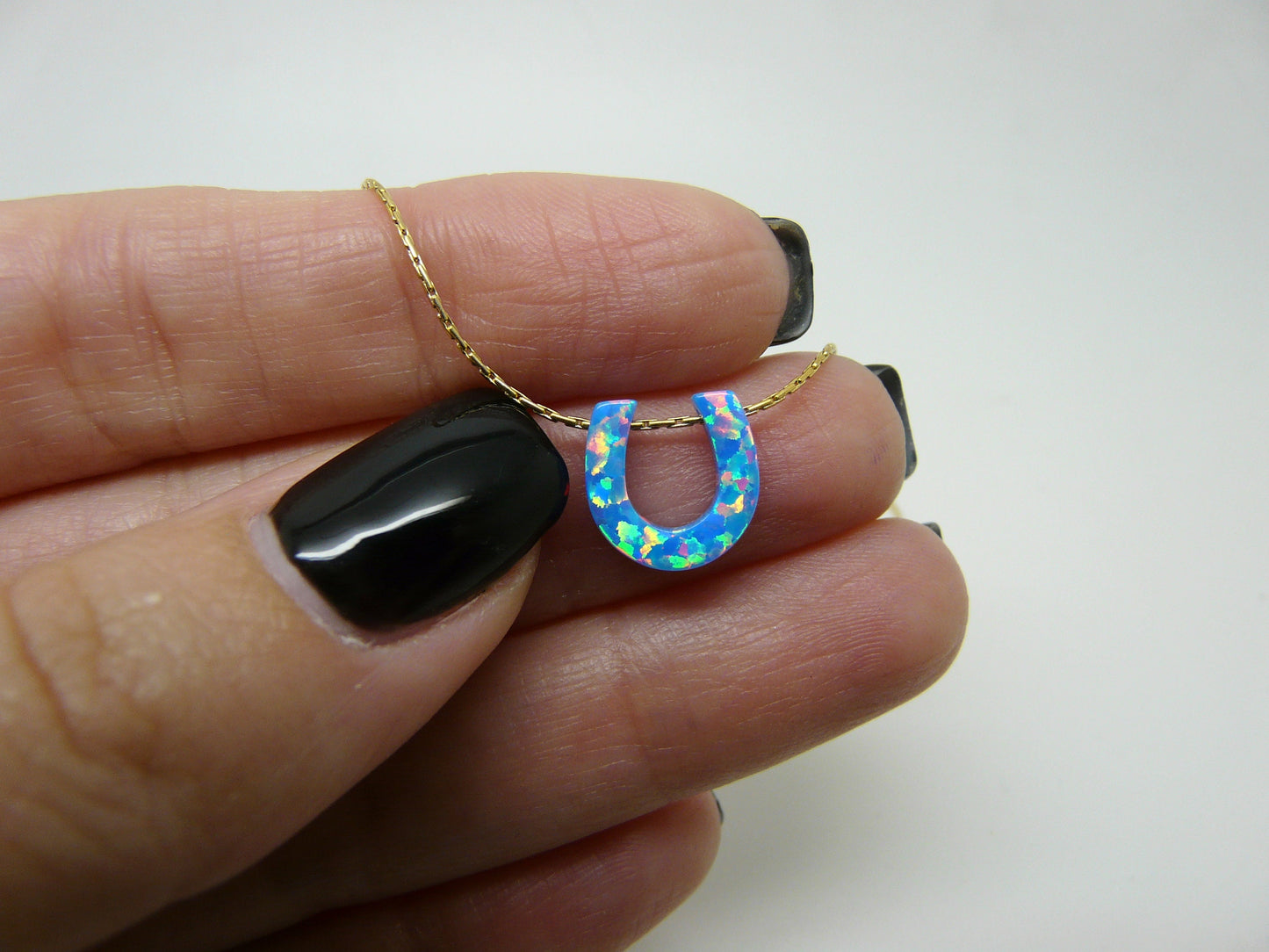 A person holding a necklace with an opal horseshoe pendant attached to a gold-filled or sterling silver chain.