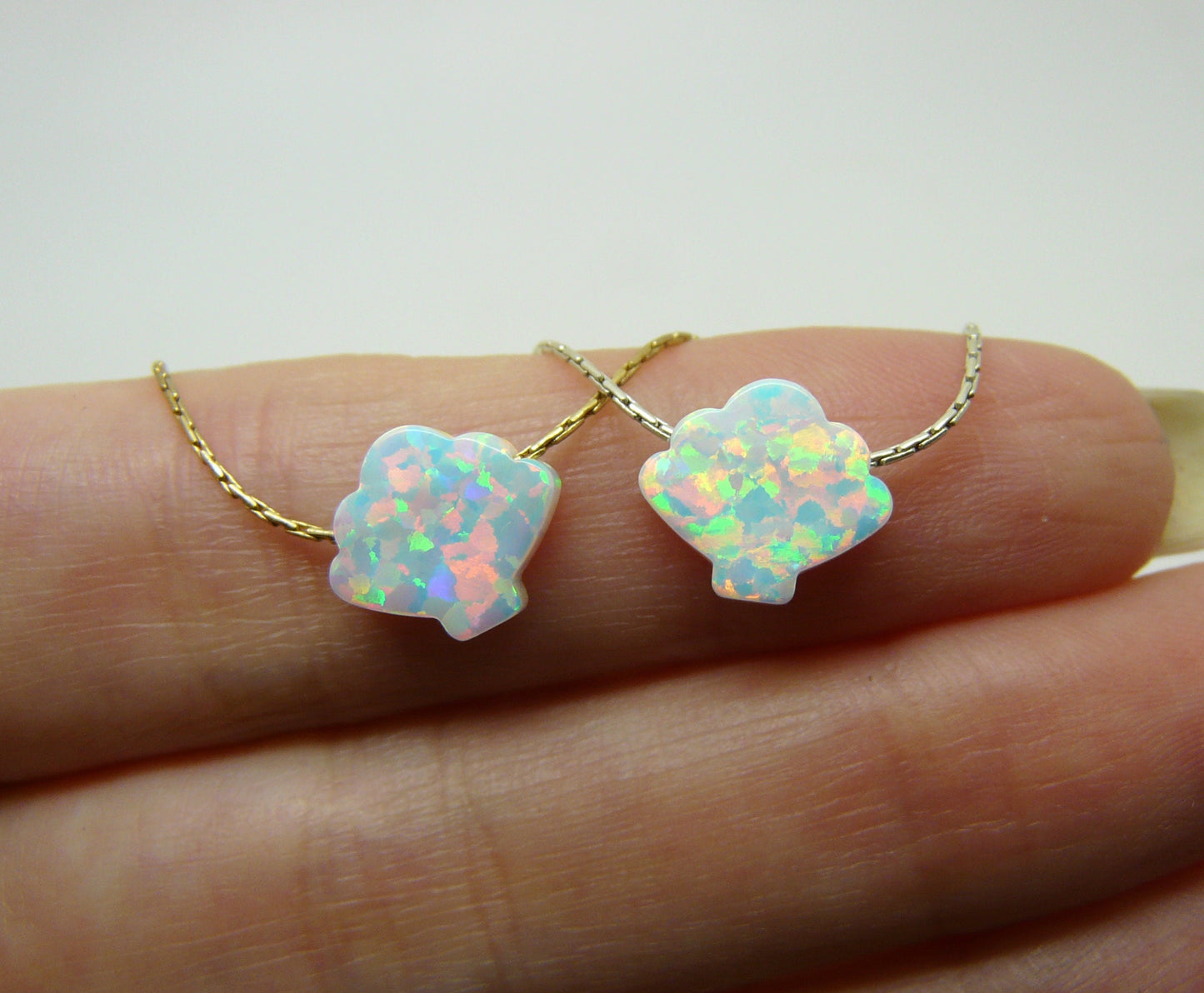 An image showing two opal shell pendants on gold chains, placed side by side on a person's finger for scale.