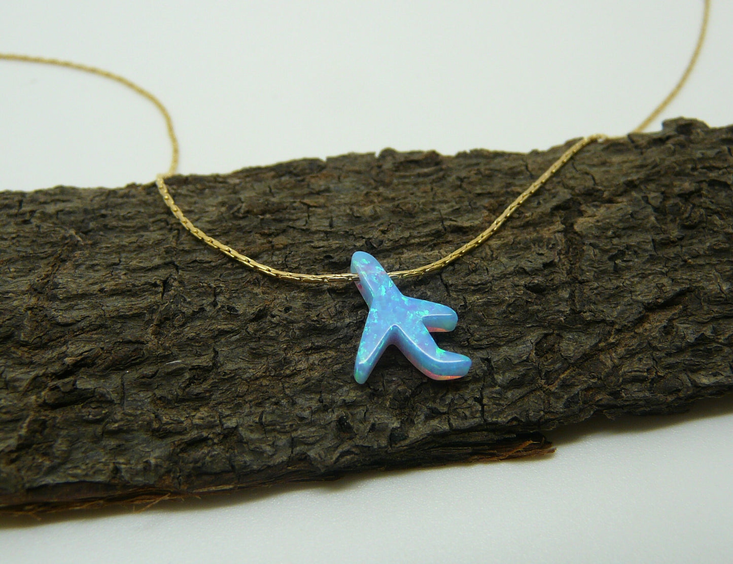 An opal airplane charm necklace placed on a wooden surface.