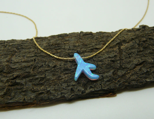 An opal airplane charm necklace placed on a wooden surface.