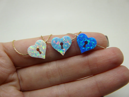A hand holding three opal heart keyhole necklaces with varying colors.