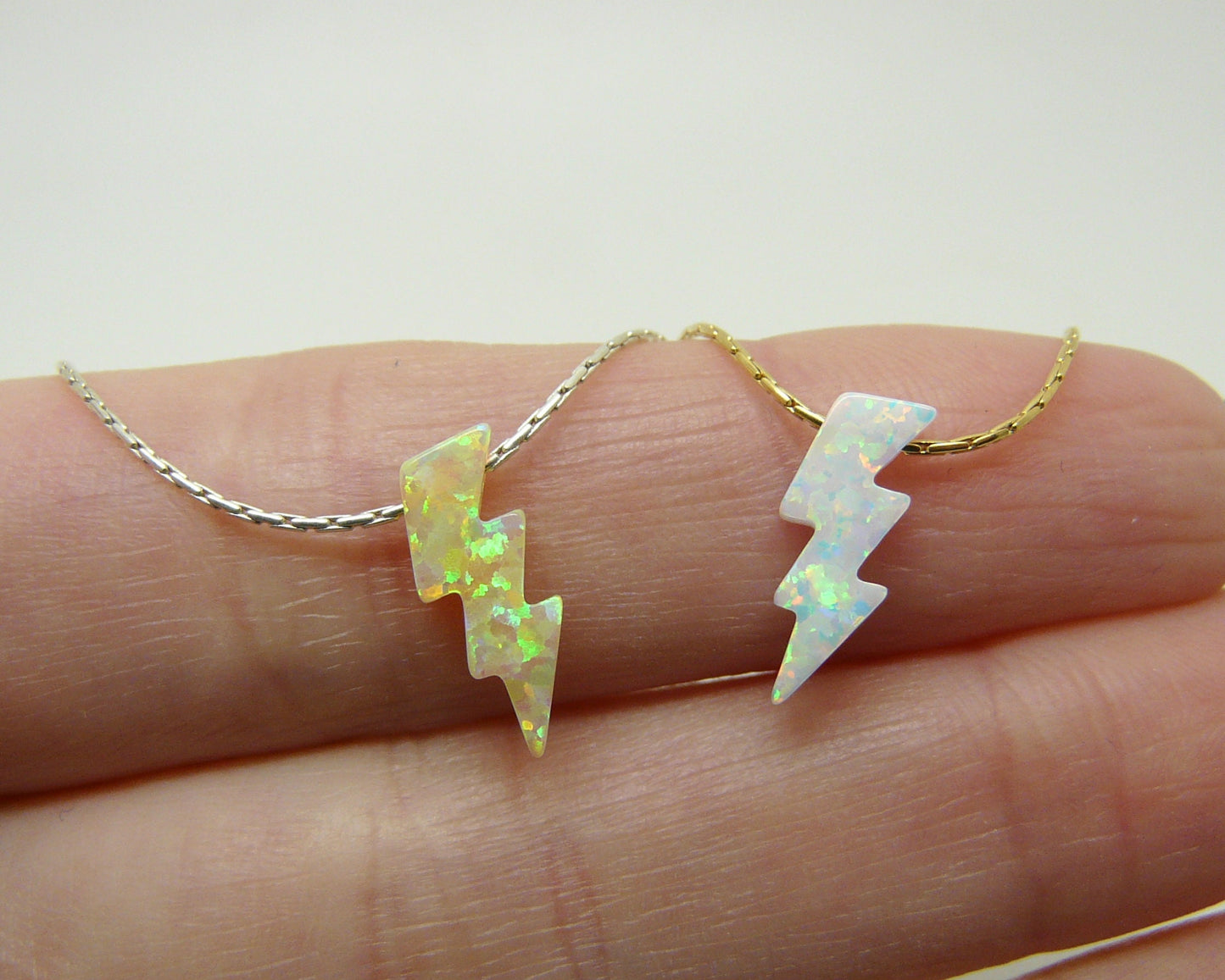 An opal lightning bolt pendant necklace displayed on a person's finger, with the pendant shown in both silver and gold filled options.
