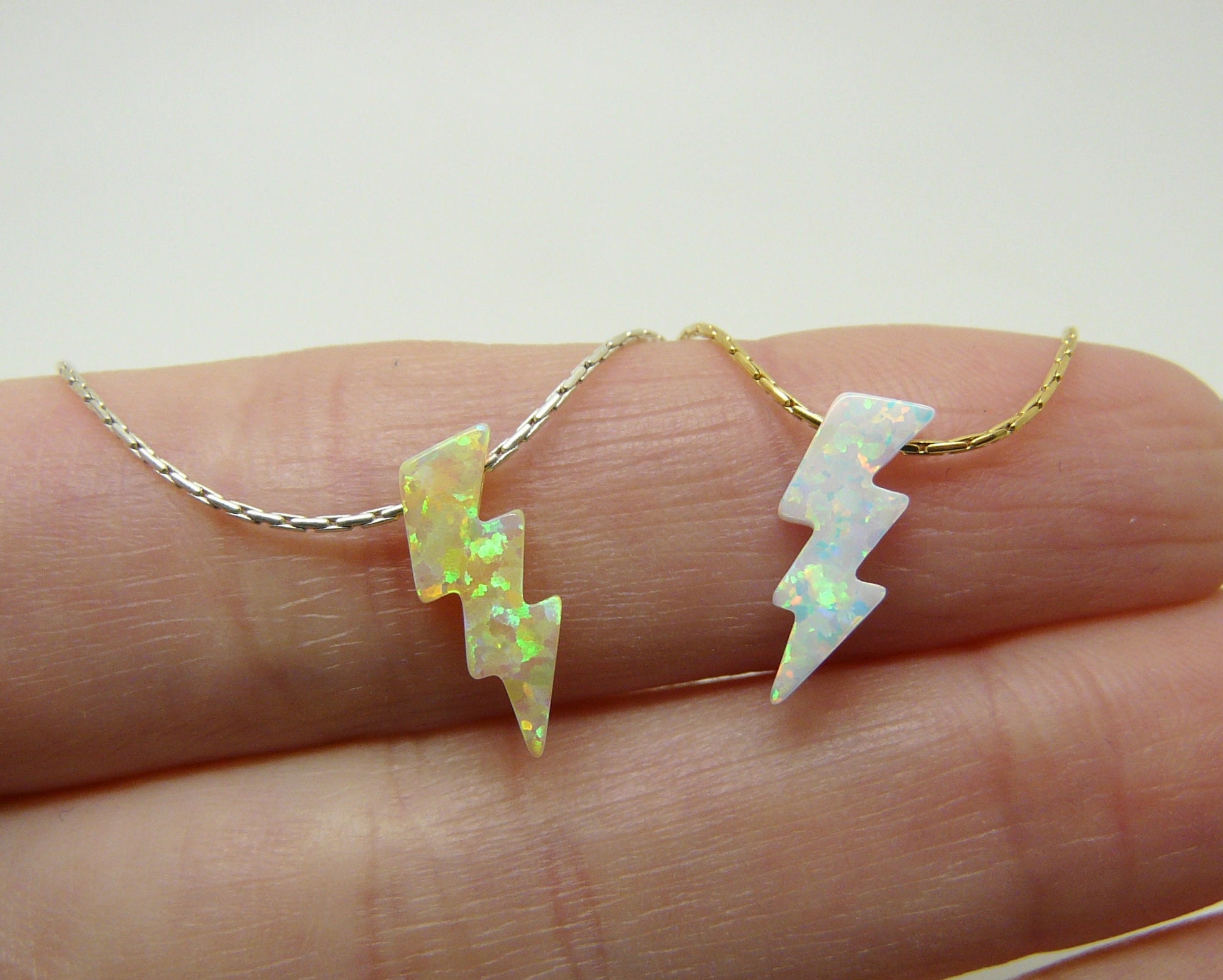 An opal lightning bolt pendant necklace displayed on a person's finger, with the pendant shown in both silver and gold filled options.