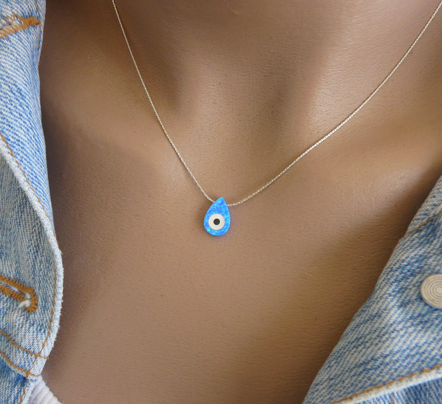A blue opal evil eye pendant necklace displayed on a mannequin wearing a denim jacket.