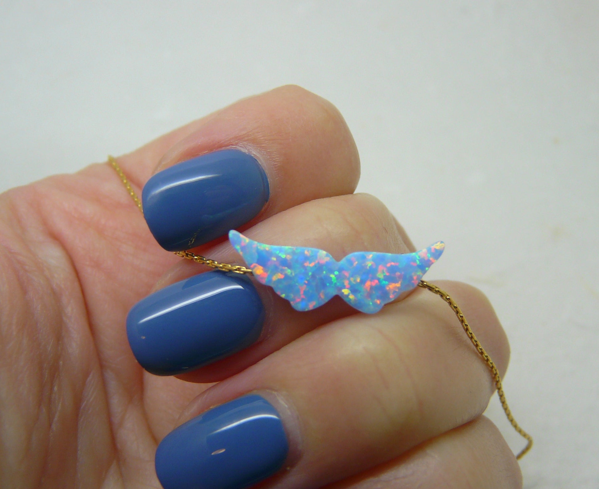 An iridescent opal angel wings pendant necklace held between fingers, with the chain visible.