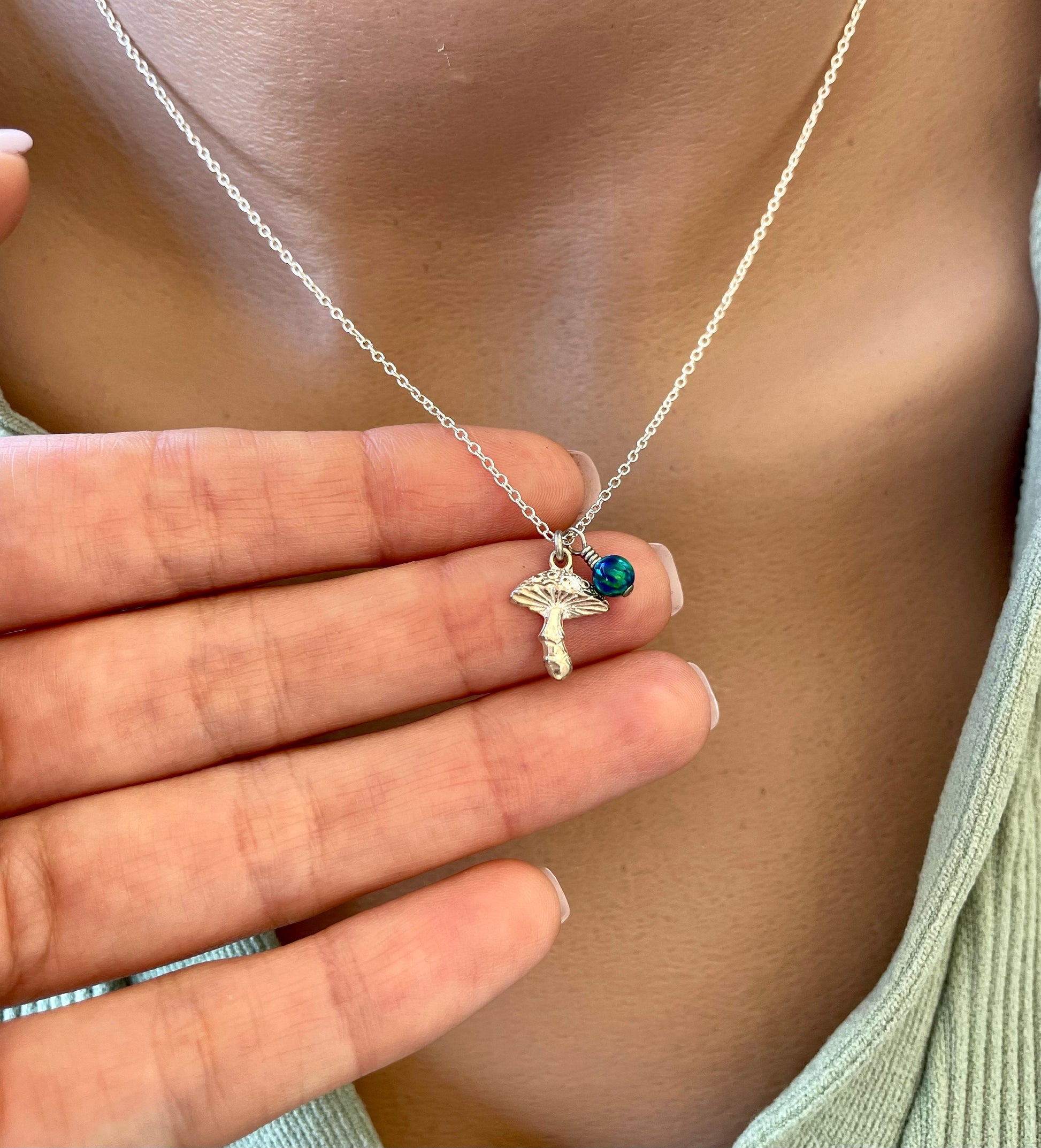 A sterling silver mushroom charm with a small opal bead accent, attached to a silver chain necklace, displayed on a person's neck.