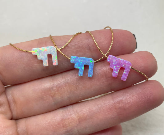 A hand holding three opal Chai necklaces with 14K gold-filled chains, displaying different shades of opal.