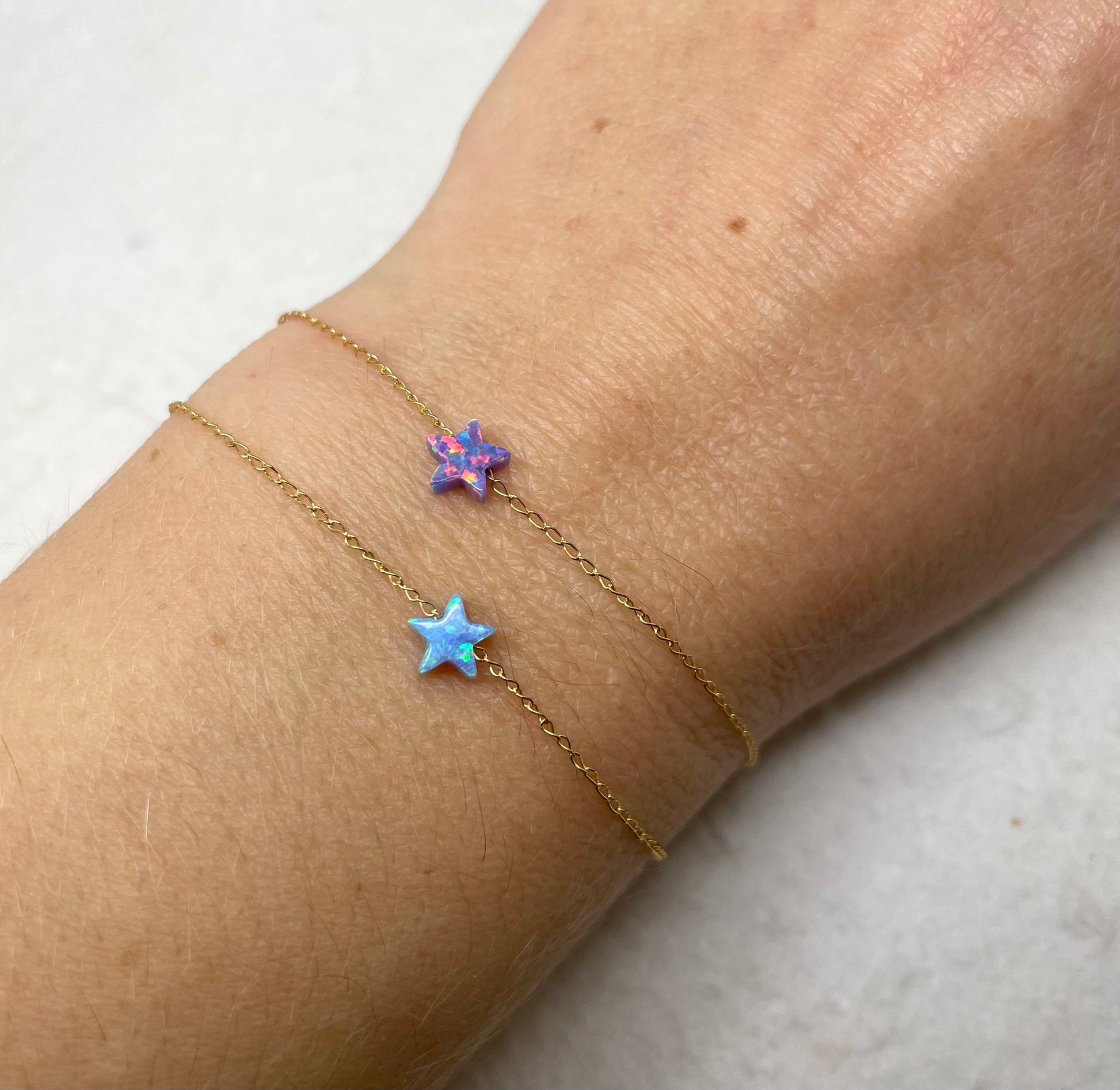 A person's wrist wearing a gold chain bracelet with two blue opal star charms.