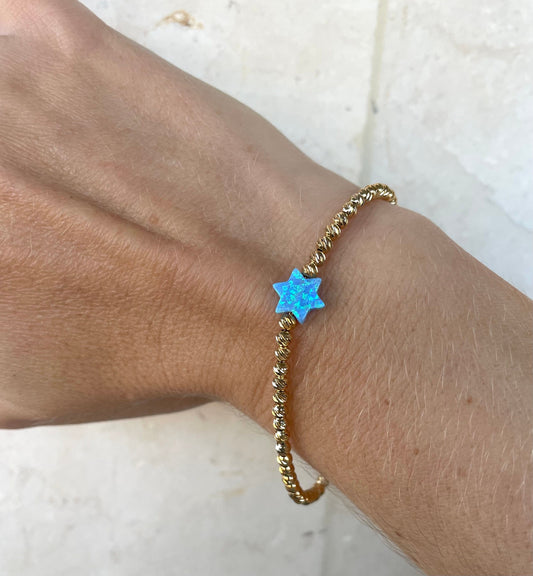 A gold-filled bracelet with a Star of David charm and blue beads on a person's wrist.