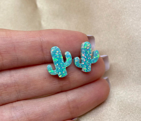 A pair of sterling silver opal cactus earrings resting on a hand, showcasing the studs with opal in snow white and aqua green colors.