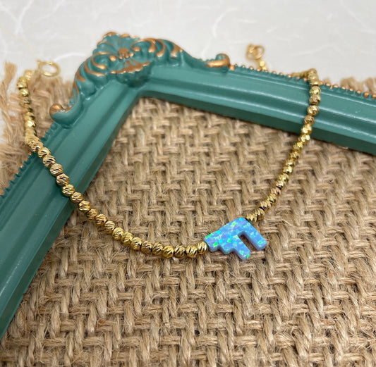 A gold-filled bracelet featuring a beaded chain and an opal chai charm, displayed on a textured background.