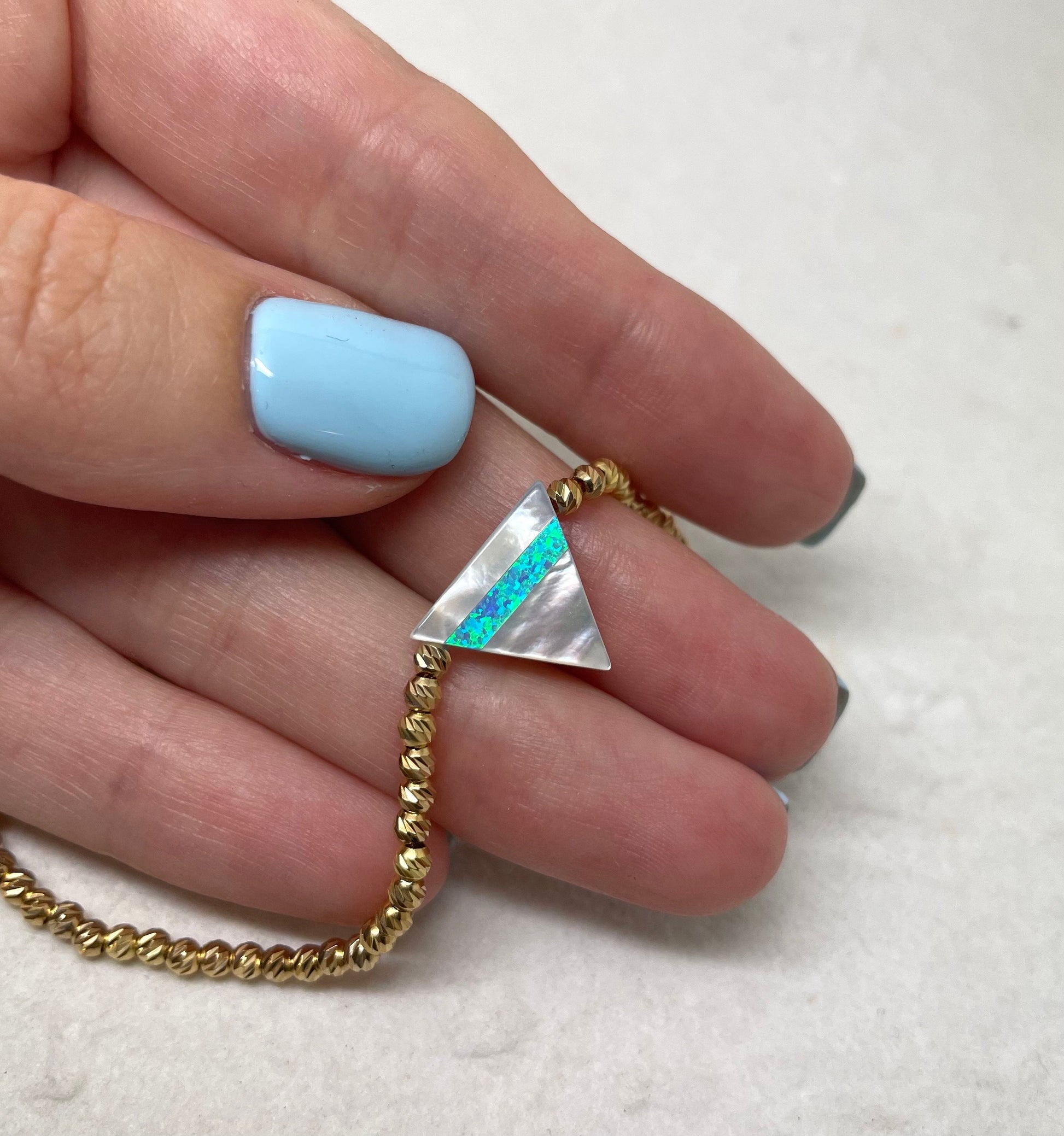 A hand holding a gold-colored triangle bracelet with a opal inlay, crafted from gold-filled components.