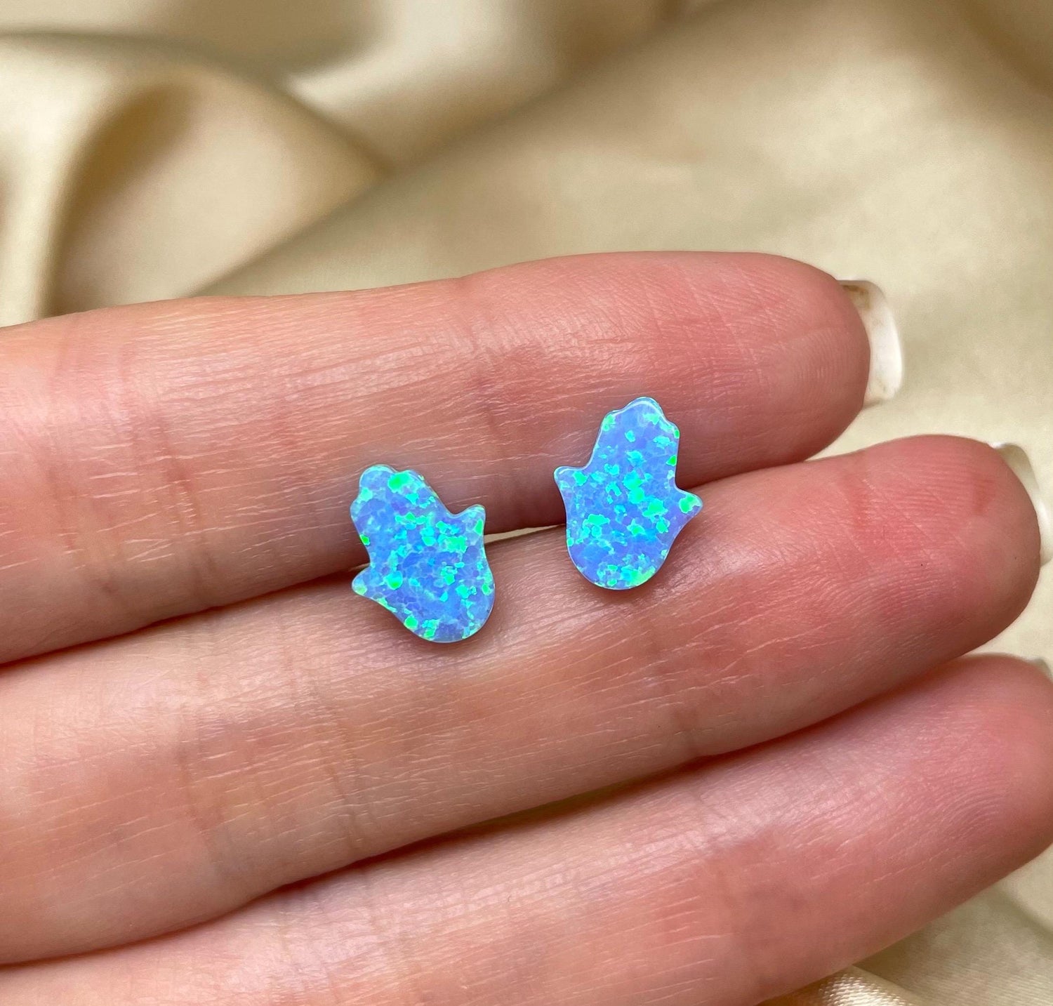 A pair of blue opal Hamsa earrings set in sterling silver, displayed on a hand.