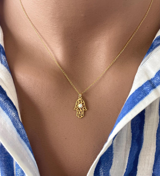 A gold-filled Hamsa hand necklace with a lab opal bead suspended on a chain, displayed on a person's neck.